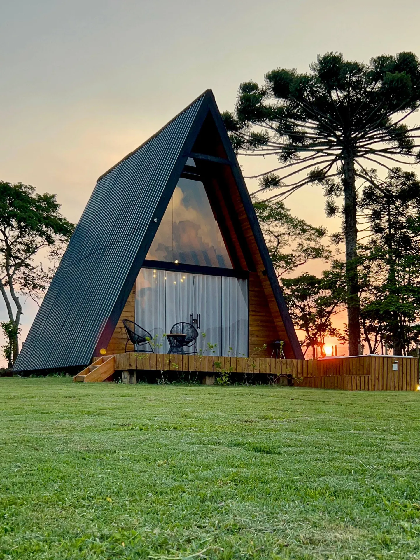 A cabana preta em A ao entardecer, com o gramado e as araucárias