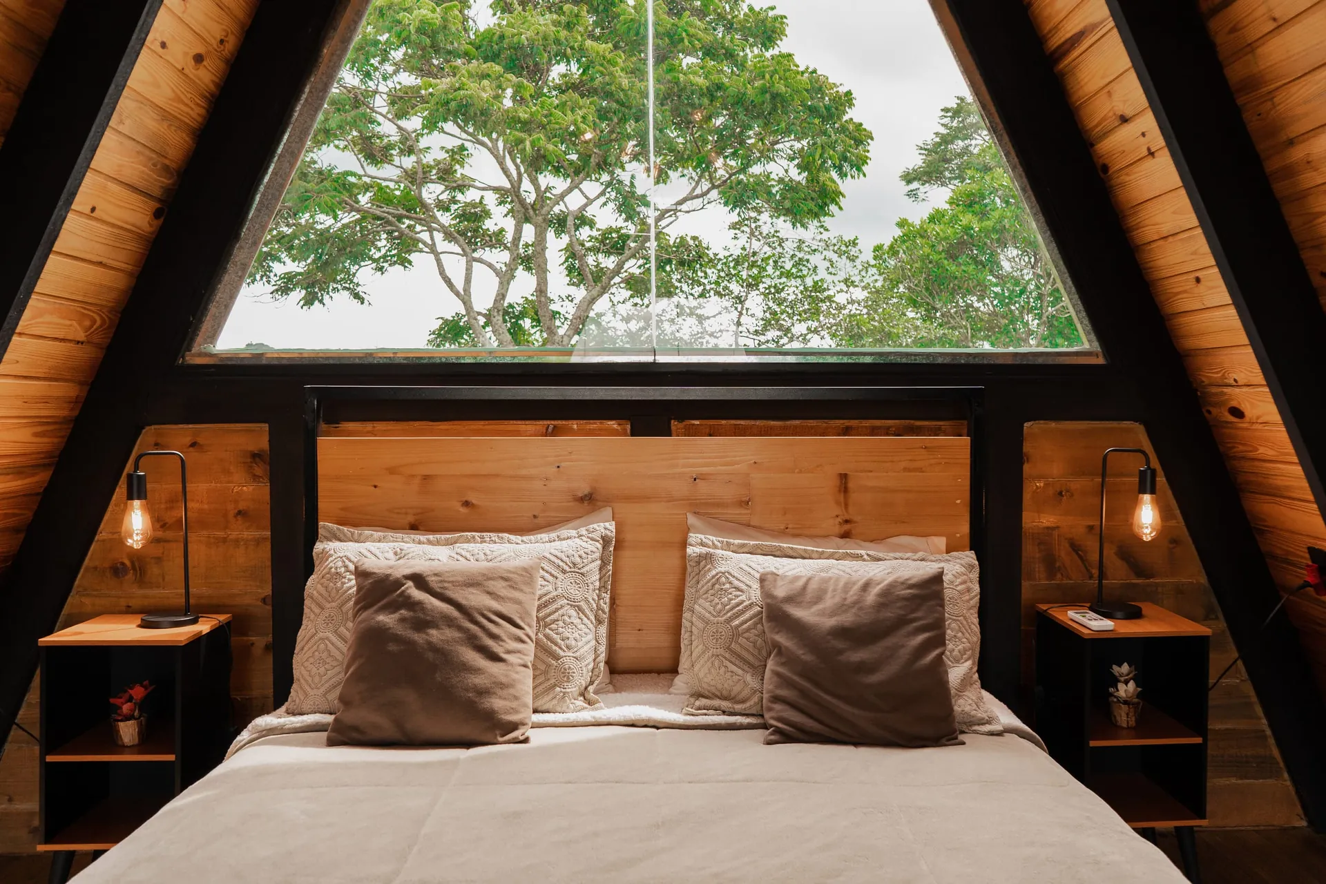 Cama queen no mezanino, com a janela triangular para as árvores